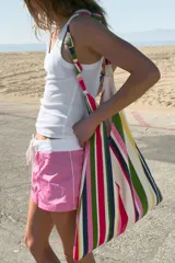 Bolsa de tejido canvas con estampado de rayas verticales en tonos rosado, verde, beige y rojo, con asa de hombro decorada con nudos.
