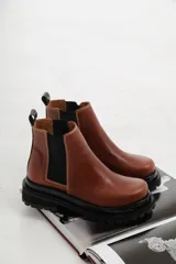 Botas tipo chelsea de cuero con suela track dentada y paneles elásticos laterales. Presentan costuras a contratono y tirador en la parte trasera.