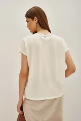 Remera de algodón color crema con estampa frontal de una bola de espejos en forma de corazón y texto en tonos rojos y negros.