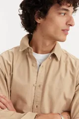 Camisa de manga larga color beige, con cuello abotonado y cierre frontal con botones.