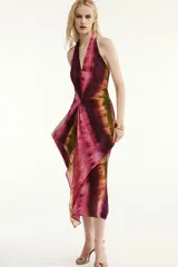 Vestido midi de cuello halter y escote en V, con diseño tie-dye en tonos fucsia, borgoña y verde. Presenta un nudo decorativo en el delantero, espalda descubierta y abertura frontal en el bajo.