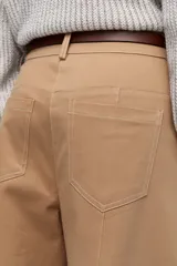 Pantalón de vestir color crema, de corte ancho y tiro alto. Se ajusta a la cintura con cinturón de cuero marrón.