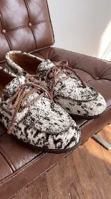 Mocasines náuticos de cuero con pelo natural con estampado animal print tipo vaca, cordones decorativos en el empeine y suela flexible.