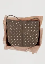 Bolso tipo hobo de gamuza marrón, adornado con tachas metálicas plateadas distribuidas por toda la superficie. Cuenta con una correa ajustable y cierre superior.