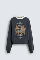 Sudadera de corte boxy fit en color gris oscuro con efecto lavado. Presenta cuello redondo en contraste color crema, manga larga con puños acanalados y estampado gráfico frontal con estrellas y tipografía estilo vintage.