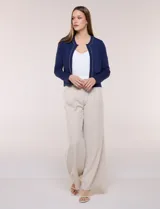 Cardigan corto azul marino de punto, con silueta entallada y largo a la cintura. Cuenta con un ribete decorativo que recorre el cuello redondo y la abertura frontal, integrando una cadena dorada en contraste. Posee bolsillos delanteros simulados y mangas largas.