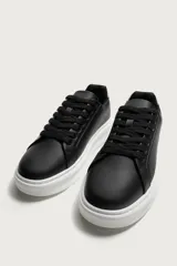Zapatilla deportiva de diseño minimalista, confeccionada en material sintético negro con suela de plataforma blanca y detalle de contraste en el talón.
