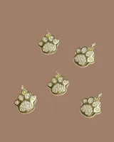 Capa de paño color rojo con corte amplio y caída natural. Presenta detalles de dijes metálicos en baño de oro distribuidos en la espalda y una etiqueta de cuero con el logo de la marca en la parte superior.