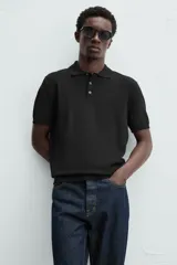 Polo de punto negro, manga corta, con cuello solapa y cierre frontal de tres botones. Presenta un calce regular y acabados en rib en mangas y ruedo.