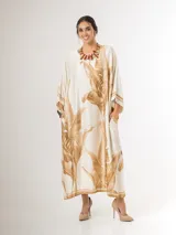 Vestido maxi túnica de corte oversized, color beige y blanco con estampa de hojas de palmera en tonos camel, mangas murciélago y bolsillos laterales.