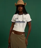 Remera estilo ringer de algodón color blanco crudo, con cuello redondo y ribetes en contraste azul marino en el cuello y mangas. Presenta un estampado frontal con la palabra "Santorini" y un gráfico estilizado.