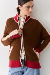 Campera de tejido de punto con cierre frontal, cuello alto y diseño color block en tonos marrón, rosa y rojo. Presenta detalles de trenzas en las mangas y puños y ruedo acanalados.