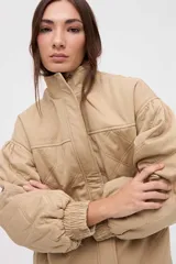 Campera bomber de gabardina con diseño capitoneado, cuello alto, cierre frontal con botones a presión ocultos y mangas abullonadas con puños elásticos.