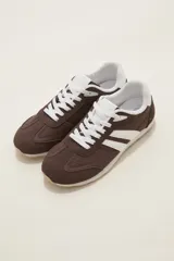 Zapatillas de estilo urbano color marrón con detalles en blanco, confeccionadas en material textil y sintético, con cordones blancos y suela de goma.