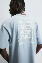 Camiseta de manga corta y cuello redondo, color celeste lavado, con estampado frontal en blanco que dice "The Mr. Rebel Dance".