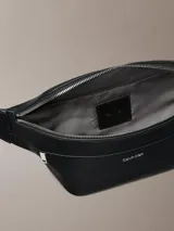 Riñonera Calvin Klein de poliuretano texturizado color negro, con cierre superior de cremallera y un bolsillo frontal con cierre. Cuenta con correa ajustable y detalles metálicos plateados.