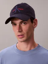 Gorra de béisbol azul marino con visera curva y parte trasera ajustable. Presenta el logo de Calvin Klein bordado en el frente con el monograma CK en azul oscuro y el nombre de la marca en rojo.