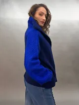 Chaqueta azul con mangas largas, cuello alto y cierre frontal con cordón. Diseño calado en el frente y mangas con patrón de rombos. Confeccionada en lana merino.