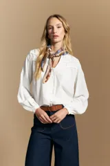 Camisa de manga larga color blanco, con cuello mao y escote en V. Presenta frunces en el canesú, cierre frontal con botones y mangas amplias con puños abotonados.