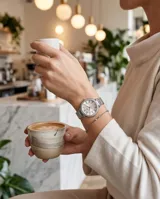 Reloj de pulsera Mini Focus con caja redonda plateada, bisel con incrustaciones de cristales y malla de acero tipo milanesa. Esfera minimalista con números romanos y movimiento de cuarzo japonés.