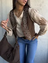 Chaleco de gamuza color chocolate con bordados decorativos en hilo claro y detalles de tachas metálicas en el frente. Presenta cierre frontal con botones forrados.