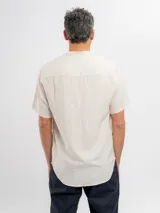 Camisa de manga corta color beige, con cuello mao, bolsillo ojal en el pecho y cierre frontal parcial con botones.
