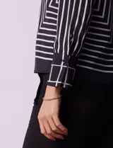 Blusa de gasa estampada con líneas verticales negras sobre fondo beige, de manga larga con puño abotonado. Espalda con abertura y botón.