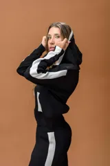 Conjunto de dos piezas compuesto por un buzo tipo hoodie con cierre frontal, capucha y bolsillos laterales, y un pantalón de corte recto. Ambas prendas son de color negro con detalles de bandas laterales en blanco.