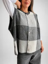 Chaleco de tejido de punto con diseño de cuadros grandes en tonos beige y gris. Presenta un corte oversize, cuello redondo y cierre frontal con botones a tono.