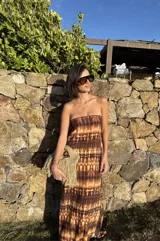 Vestido largo strapless, ajustado al cuerpo, con estampado batik en tonos marrones y naranjas.