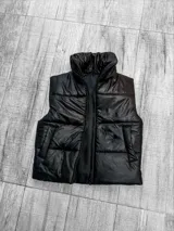 Chaleco puffer negro con cuello alto y cierre frontal con cremallera. Tiene bolsillos laterales y diseño acolchado.