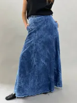 Falda larga de jean denim con efecto de lavado ácido y diseño de paneles geométricos cosidos. Presenta cintura alta, cierre lateral invisible y bolsillos ocultos, con un corte acampanado que aporta volumen y movimiento.
