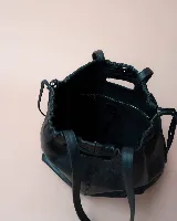 Cartera tipo tote de cuero color bordó, con diseño fruncido en los laterales y abertura central integrada como asa. Presenta una silueta flexible y espaciosa, ideal para uso diario.