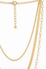 Collar de tres tiras de cadena dorada con diferentes diseños: una cadena fina de eslabones clásicos, una tira plana tipo escama de pescado y una cadena con eslabones en forma de trébol o flor.
