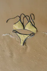 Conjunto de bikini color amarillo con ribetes en contraste color azul marino. El corpiño es de estilo triangular con tiras finas y la bombacha es de corte semivedetina con tiras laterales ajustables.