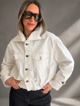 Campera bomber de denim blanco, confeccionada en mezcla de algodón y poliéster, con silueta relajada y largo a la cintura. Cuenta con cuello amplio, bolsillos delanteros con solapa, cierre frontal con botones y cintura elastizada.