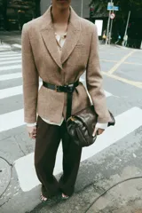 Blazer de corte clásico con cuello solapa y manga larga, confeccionado en tejido con patrón de espiga en tonos tierra y líneas verticales en color salmón. Cuenta con bolsillos delanteros y cierre frontal con botones ocultos.