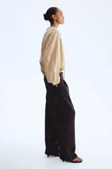 Pantalón de corte holgado en sarga color marrón oscuro. Modelo de tiro alto con trabilla ajustable de botón a ambos lados de la pretina, cierre con corchete oculto, piernas barrel con pinzas, pliegues adelante y atrás, bolsillos al bies y bolsillos traseros decorativos.