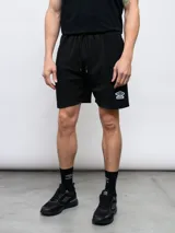 Bermuda de felpa negra con efecto lavado, corte recto y cordón ajustable en la cintura. Presenta un panel vertical en la parte delantera de cada pierna y el logo Umbro bordado en blanco en el muslo izquierdo.