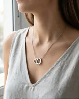 Collar de acero con cadena fina y dos dijes entrelazados, uno en forma de corazón y otro circular.