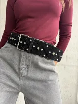 Faja ancha de gamuza negra con diseño de tiras entrecruzadas y tachas metálicas plateadas. Cuenta con hebilla metálica rectangular.