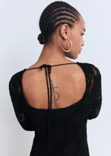 Vestido corto de crochet negro con cuello redondo y mangas largas acampanadas. Presenta una espalda abierta con cierre de lazo y cuenta con forro interior.