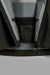 Cazadora deportiva de esquí con diseño bicolor en tonos negro y verde oliva. Presenta capucha amplia con visera, cierre frontal con cremallera termosellada, bolsillos frontales y en manga con cierres impermeables, y aberturas de ventilación en las axilas. Incluye faldón interior antinieve, puños ajustables y tecnología de rescate RECCO.