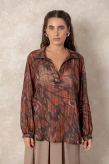 Blusa de gasa con estampado abstracto en tonos verdes y marrones, con detalles de hilos dorados. Presenta cuello camisero con escote en V, mangas largas con puños elásticos y un corte holgado.