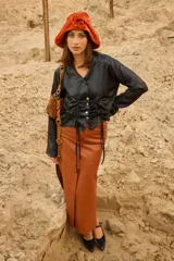 Falda larga de cuero color mostaza, de tiro bajo y silueta recta con tajos delanteros y laterales, bolsillos funcionales y cierre de botón.