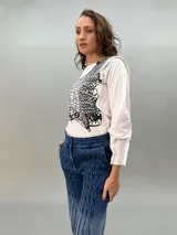 Remera negra de algodón con estampado dorado que simula un tejido o collar sobrepuesto. Presenta una moldería que realza los hombros y se entalla levemente hacia la cintura.