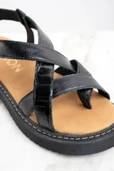 Sandalia de cuero color negro charol, con tiras cruzadas y hebilla ajustable al tobillo. Plataforma con suela track.