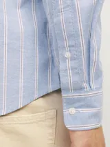 Camisa de vestir de manga larga con cuello abotonado y bolsillo frontal. Presenta un diseño de rayas verticales en tonos azul y blanco, con cierre frontal de botones.