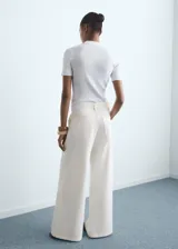 Jeans wide leg de tiro medio color blanco marfil, con diseño largo, trabillas para cinturón, cierre de botón y cremallera, cuatro bolsillos y detalle de pinzas delanteras.