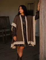 Ruana de lana merino y mohair color marrón, con diseño de caída fluida y calce amplio. Presenta terminaciones artesanales de encaje tejido en color crema en los bordes.